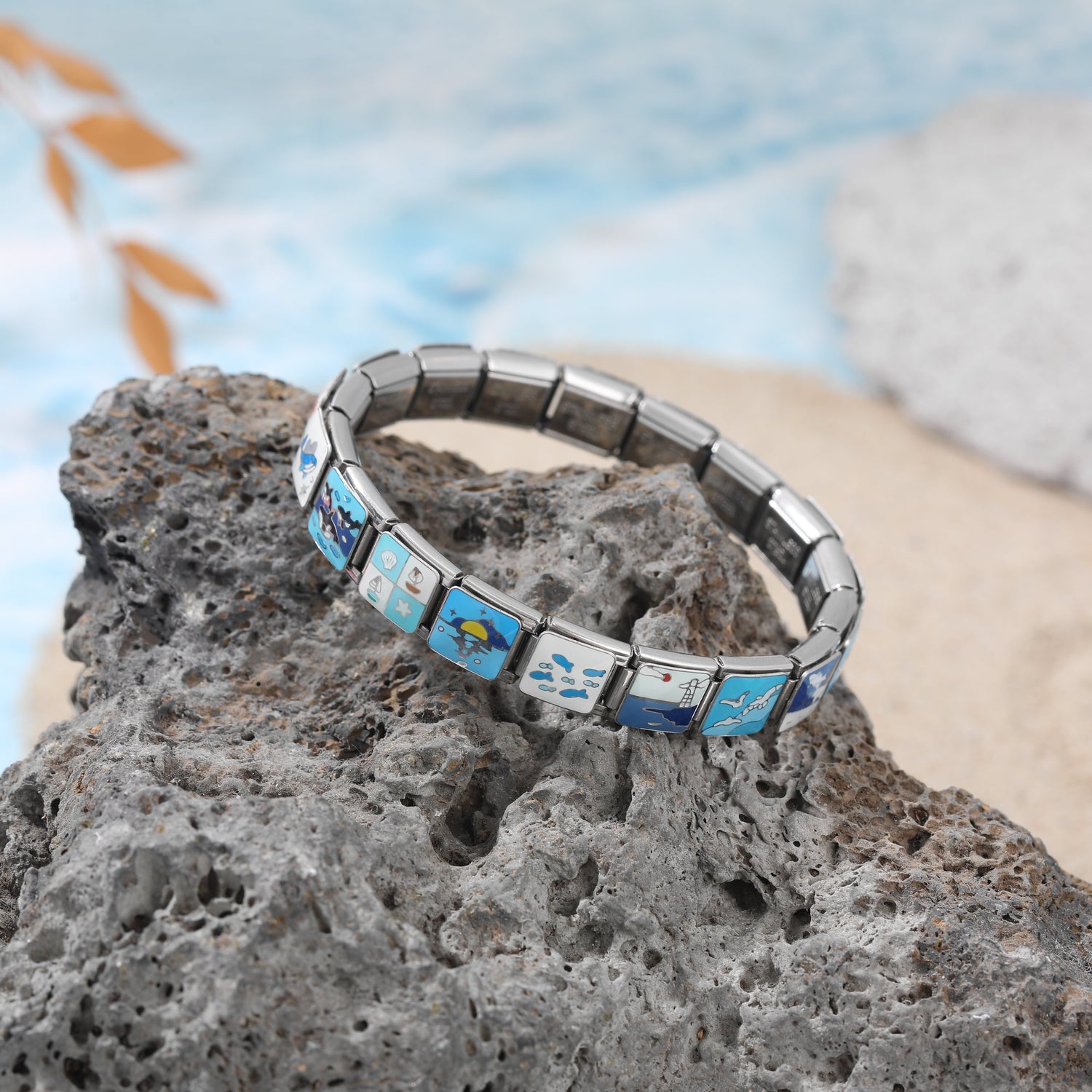 Italian charm bracelet with ocean-themed charms displayed on stone slabs, featuring blue sea and marine symbol links