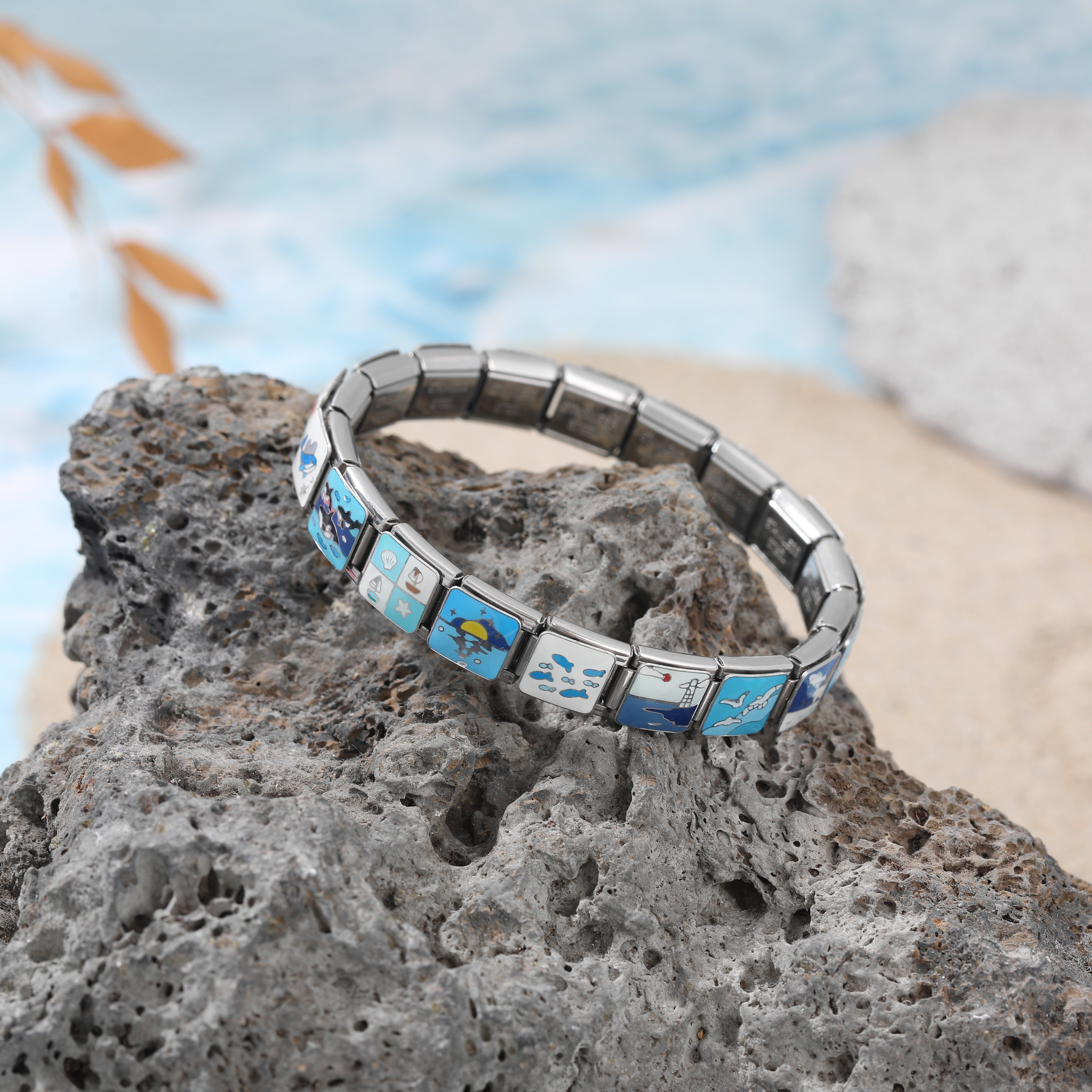 Italian charm bracelet with ocean-themed charms displayed on stone slabs, featuring blue sea and marine symbol links