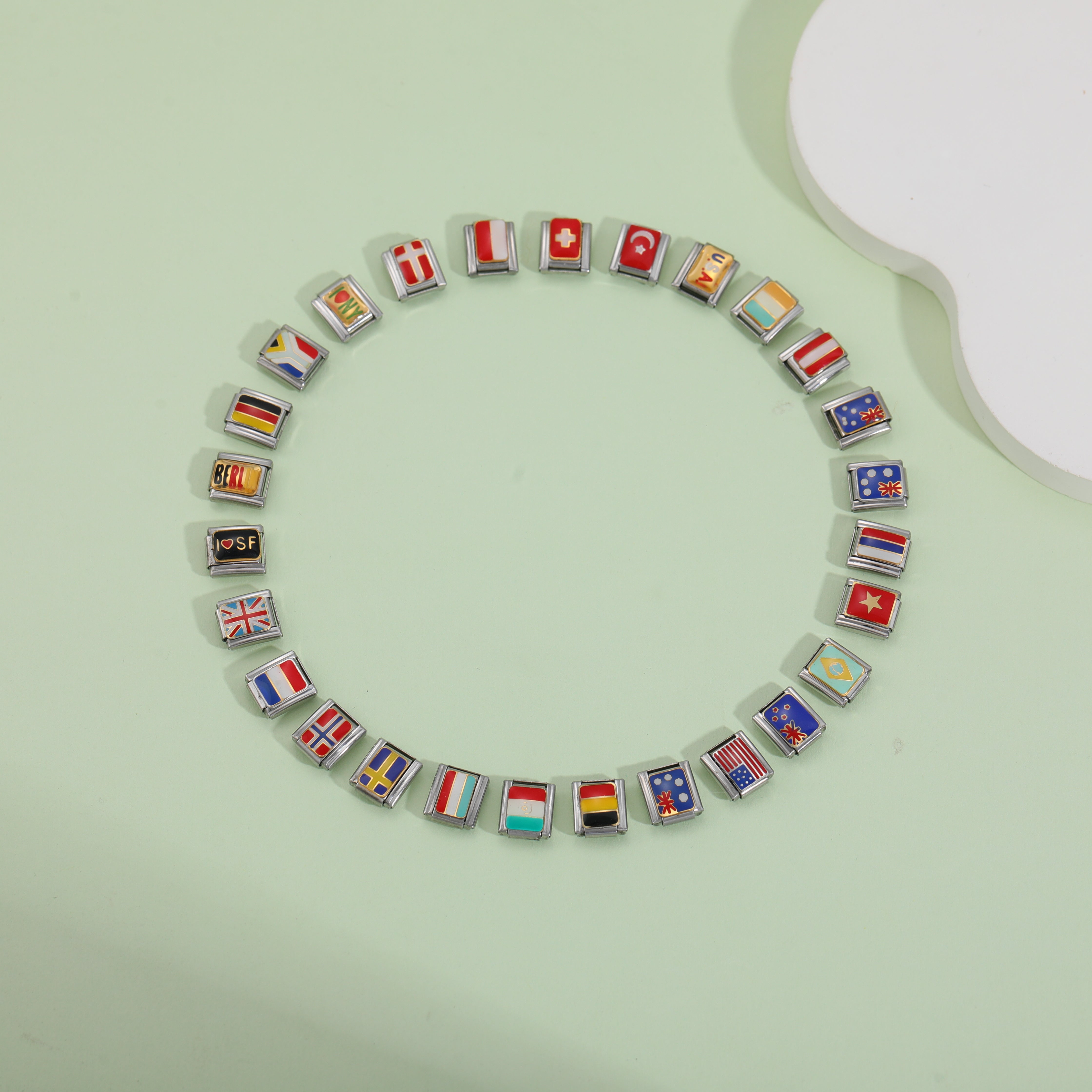 Italian charm bracelet with colorful country flag charm links arranged in a circle on green background