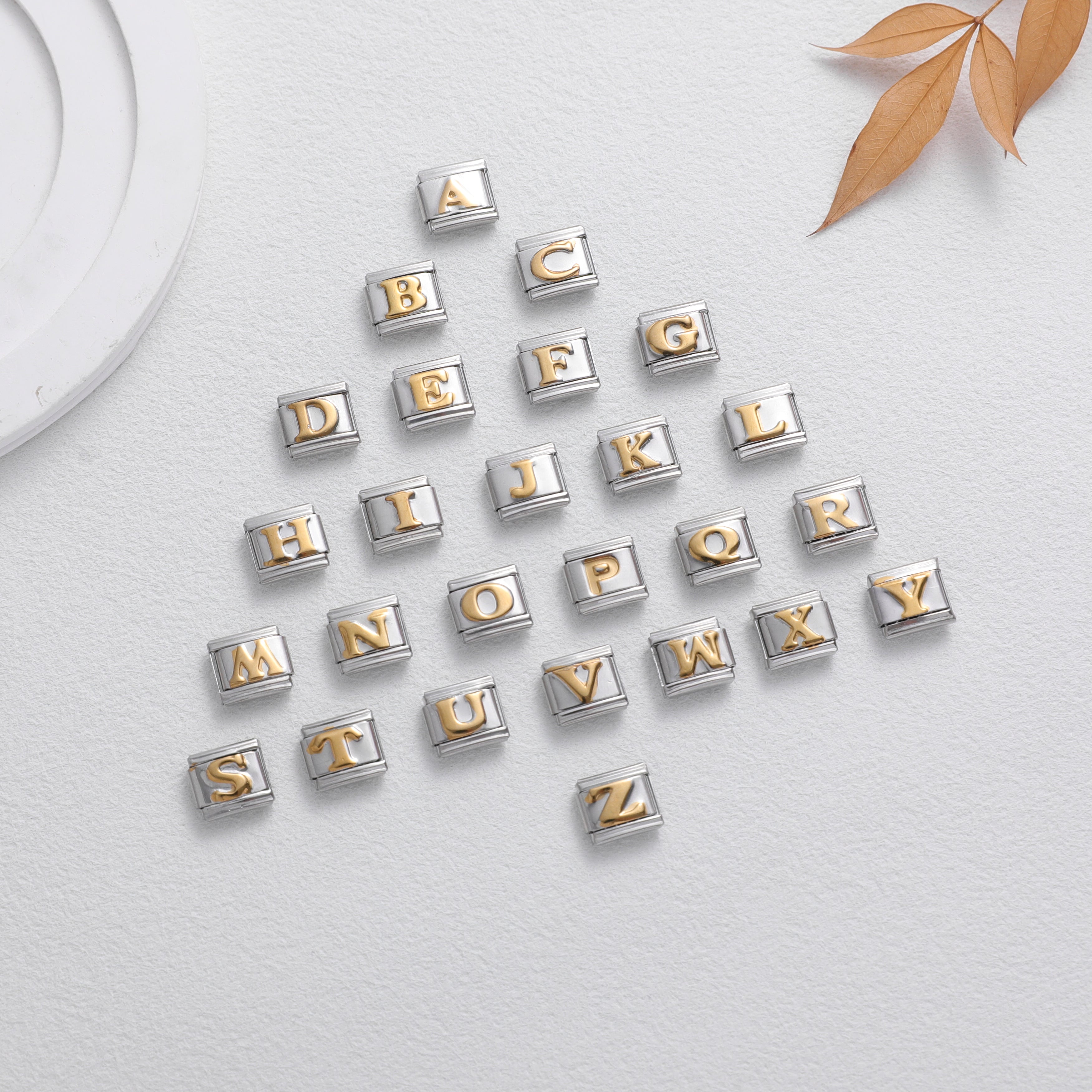Gold letter alphabet charms for Italian charm bracelet arranged in a triangle on a light neutral background