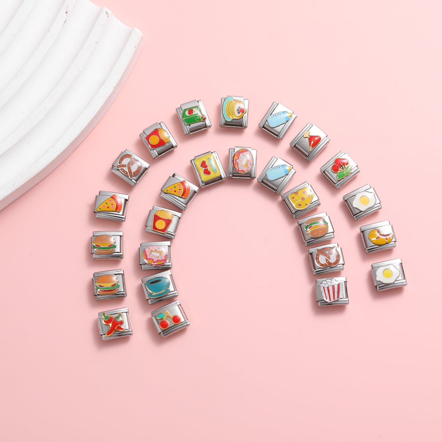 Food-themed Italian charm bracelet links arranged in a rainbow shape on a pink background