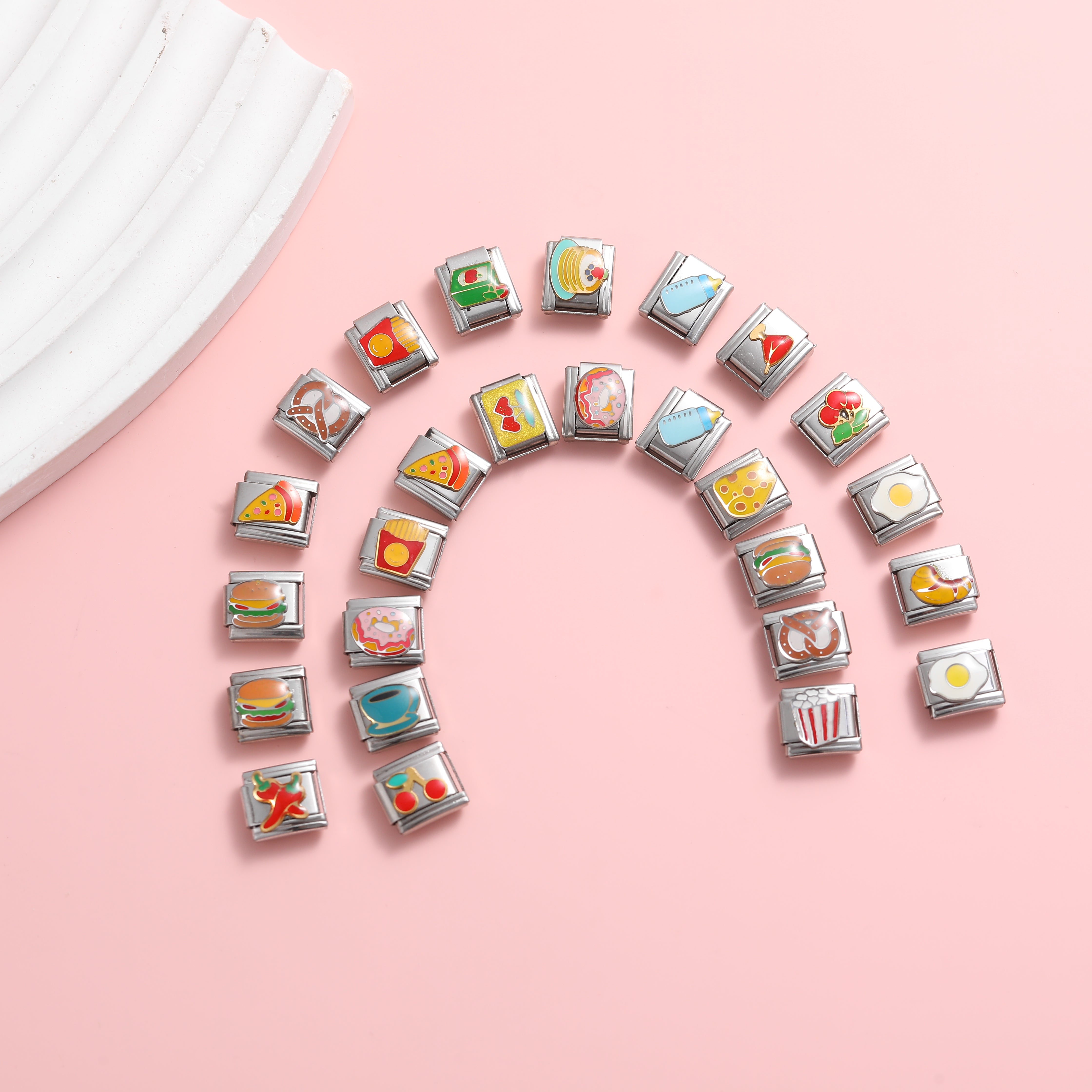 Food-themed Italian charm bracelet links arranged in a rainbow shape on a pink background