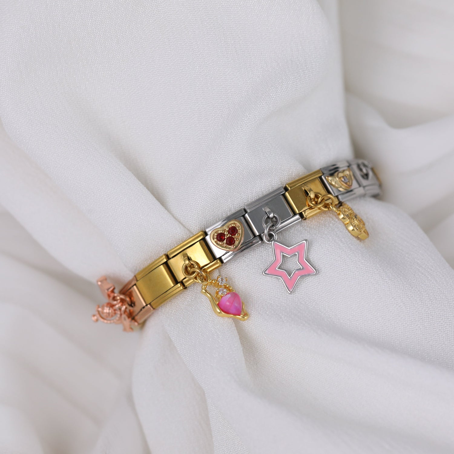 Italian charm bracelet with gold links and pink star and heart dangling charms displayed on soft fabric