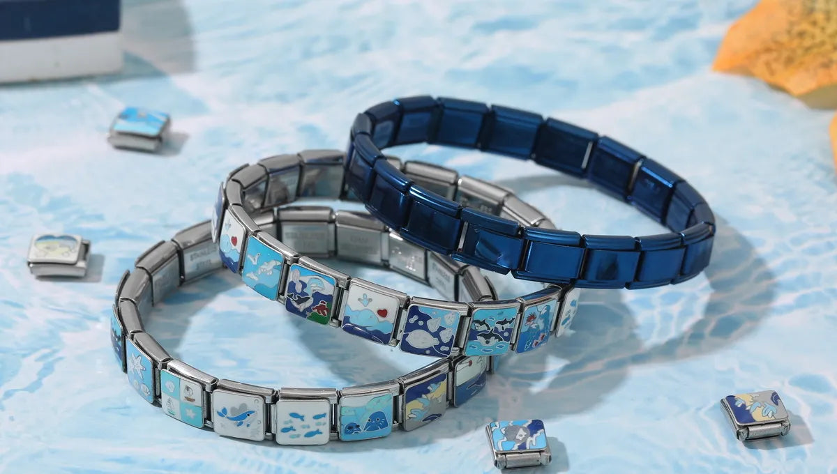 Three custom Italian charm bracelets stacked in a converging layout, with scattered stainless steel letter and symbol charms nearby – CHARMSDIY