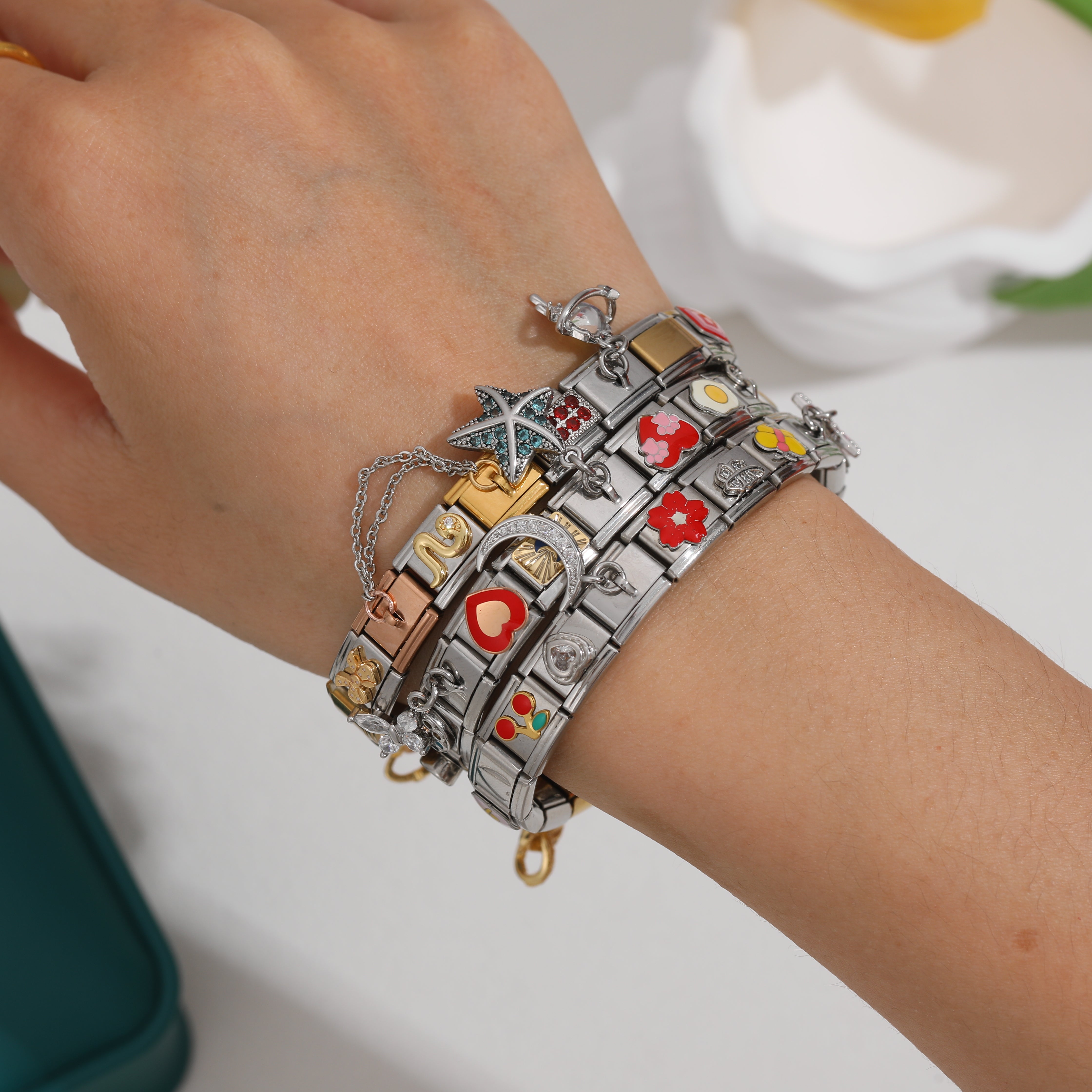 Close-up of a hand wearing stacked Italian charm bracelets with colorful enamel charms, starfish and heart designs