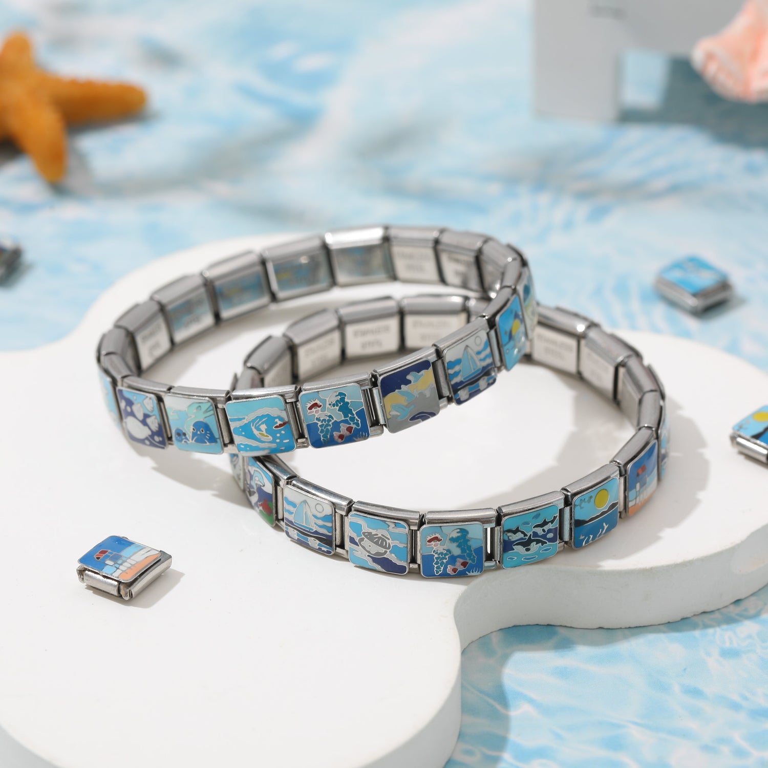 Double-layer Italian charm bracelet with ocean-inspired blue enamel charms displayed on a white platform