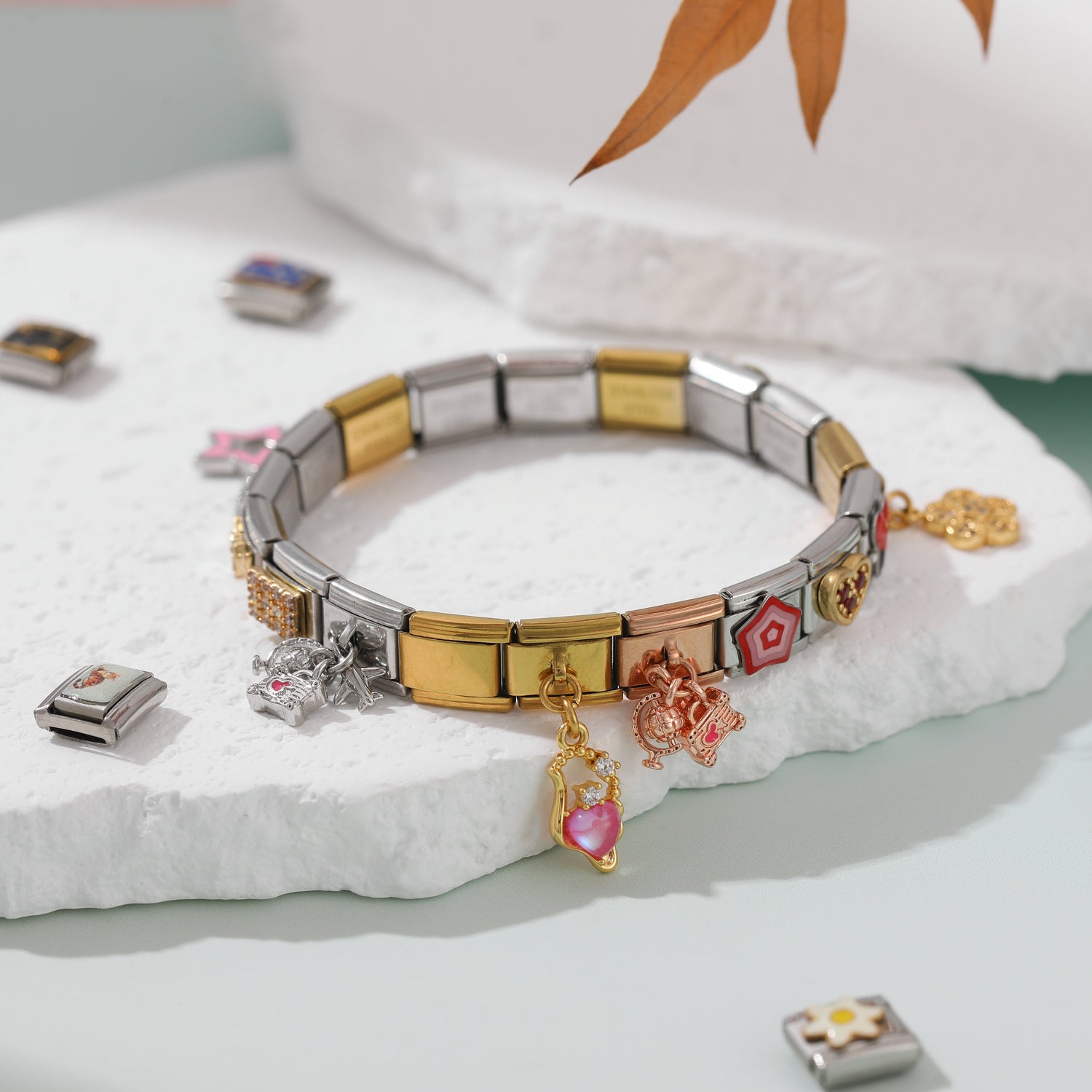 Italian charm bracelet with mixed charms and dangling pendants displayed on a white stone platform