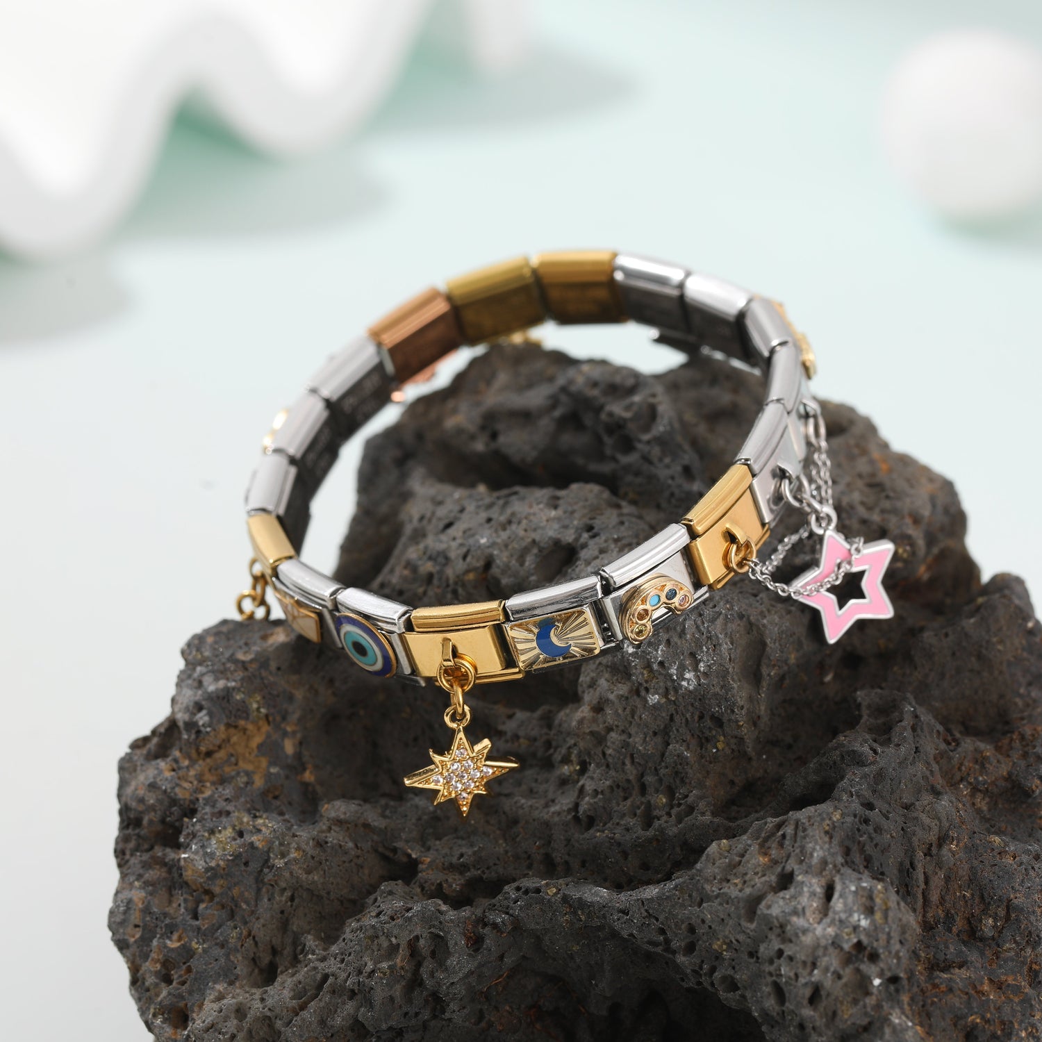 Italian charm bracelet with gold and silver links and dangling star charms displayed on a natural stone background