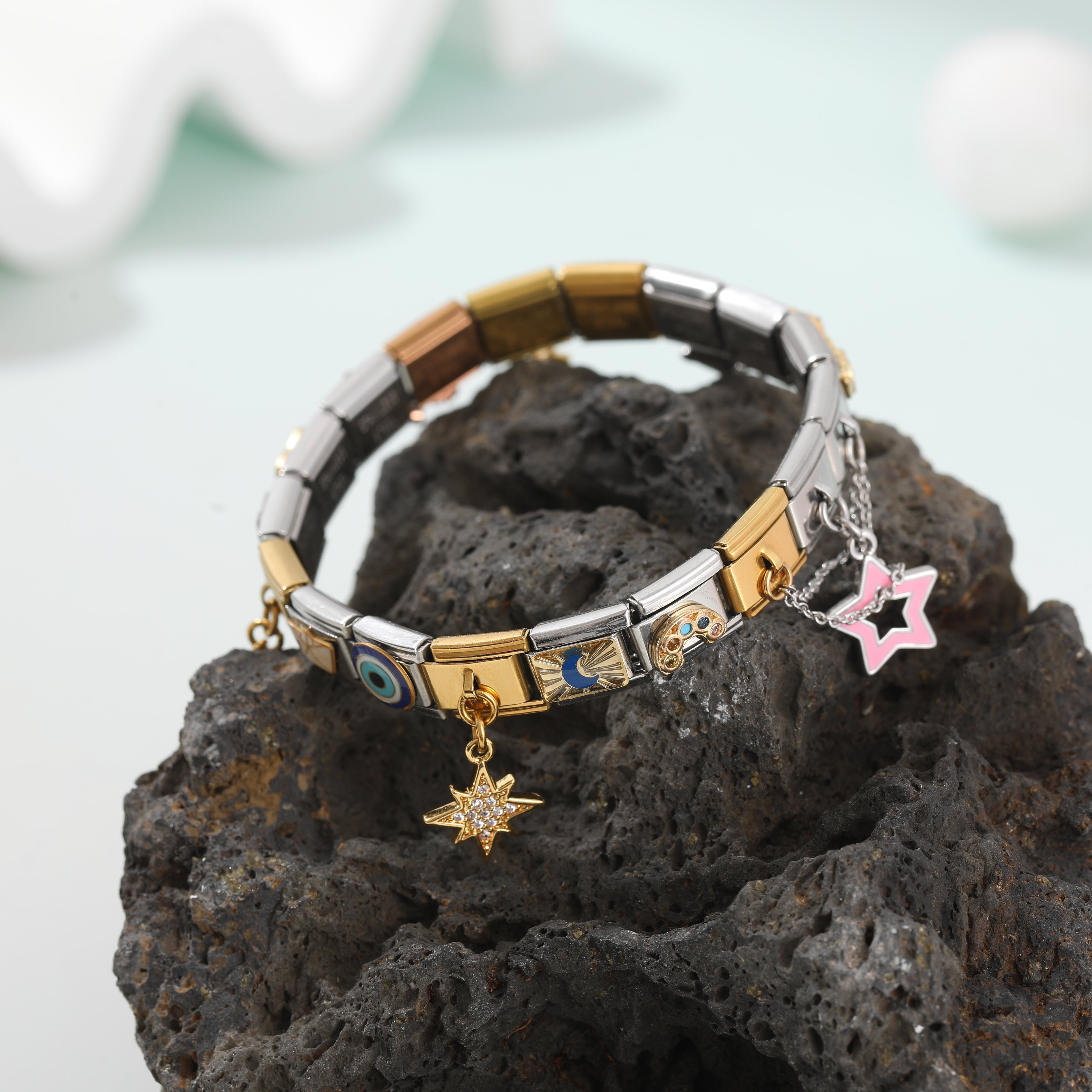 Italian charm bracelet with gold and silver links and dangling star charms displayed on a natural stone background