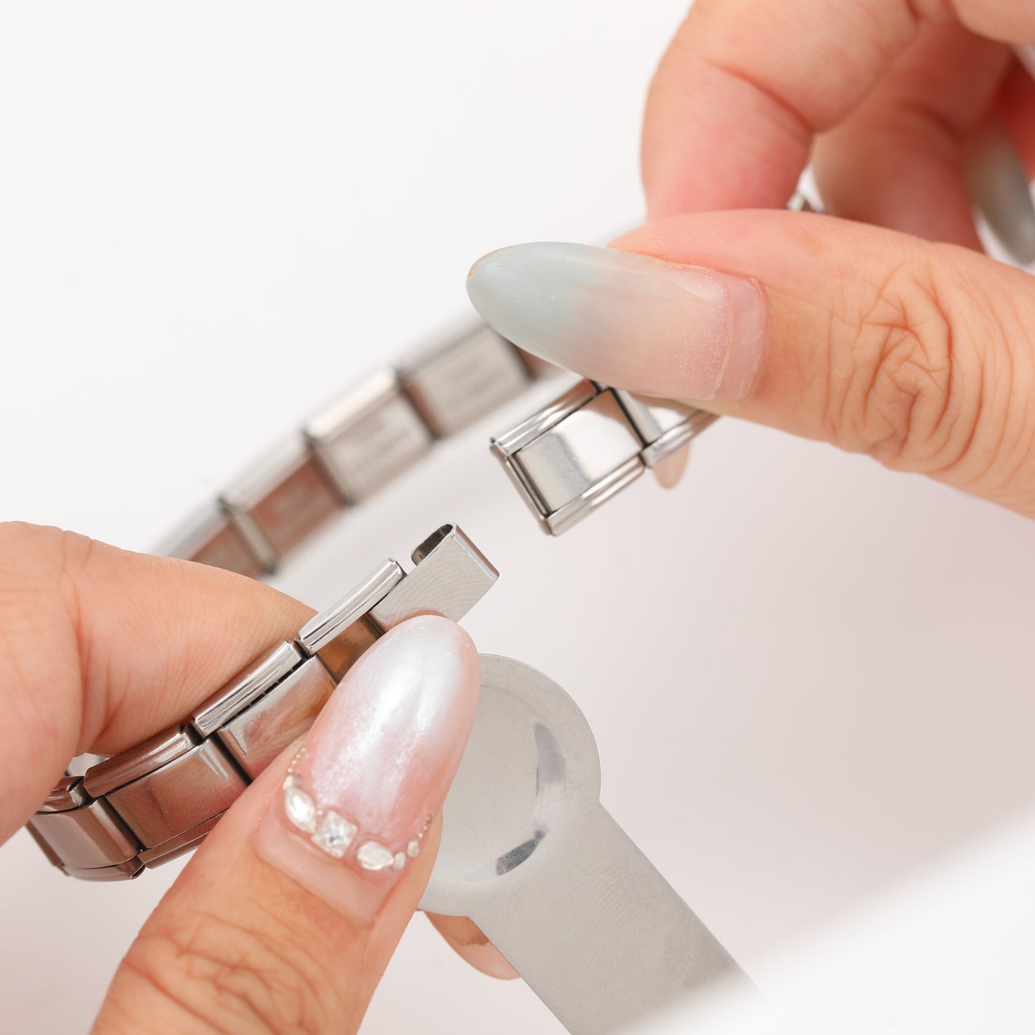 Close-up detail of an Italian charm bracelet link being opened, showing the expandable spring mechanism.