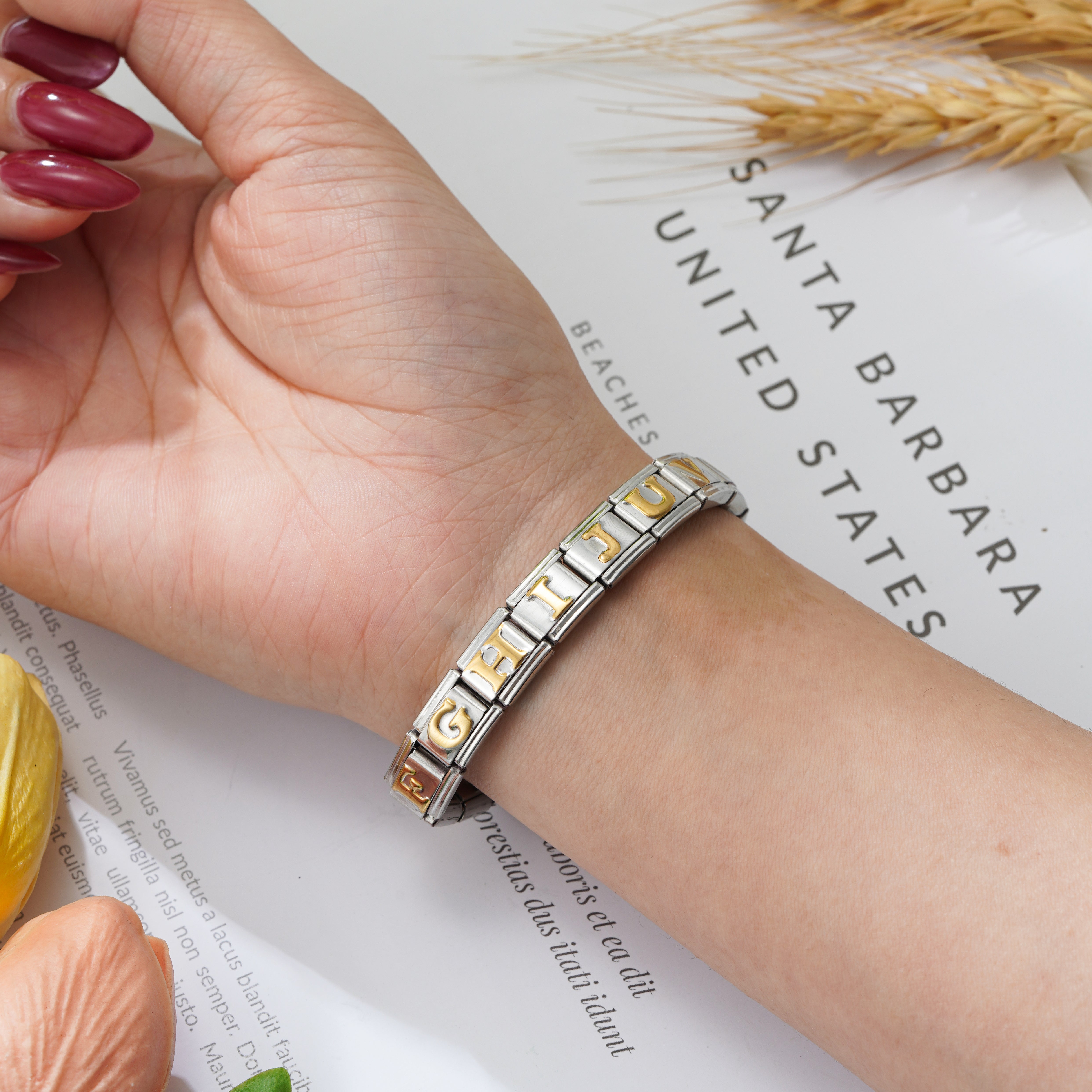 A close-up of a stainless steel Italian charm bracelet with gold initial links on the wrist