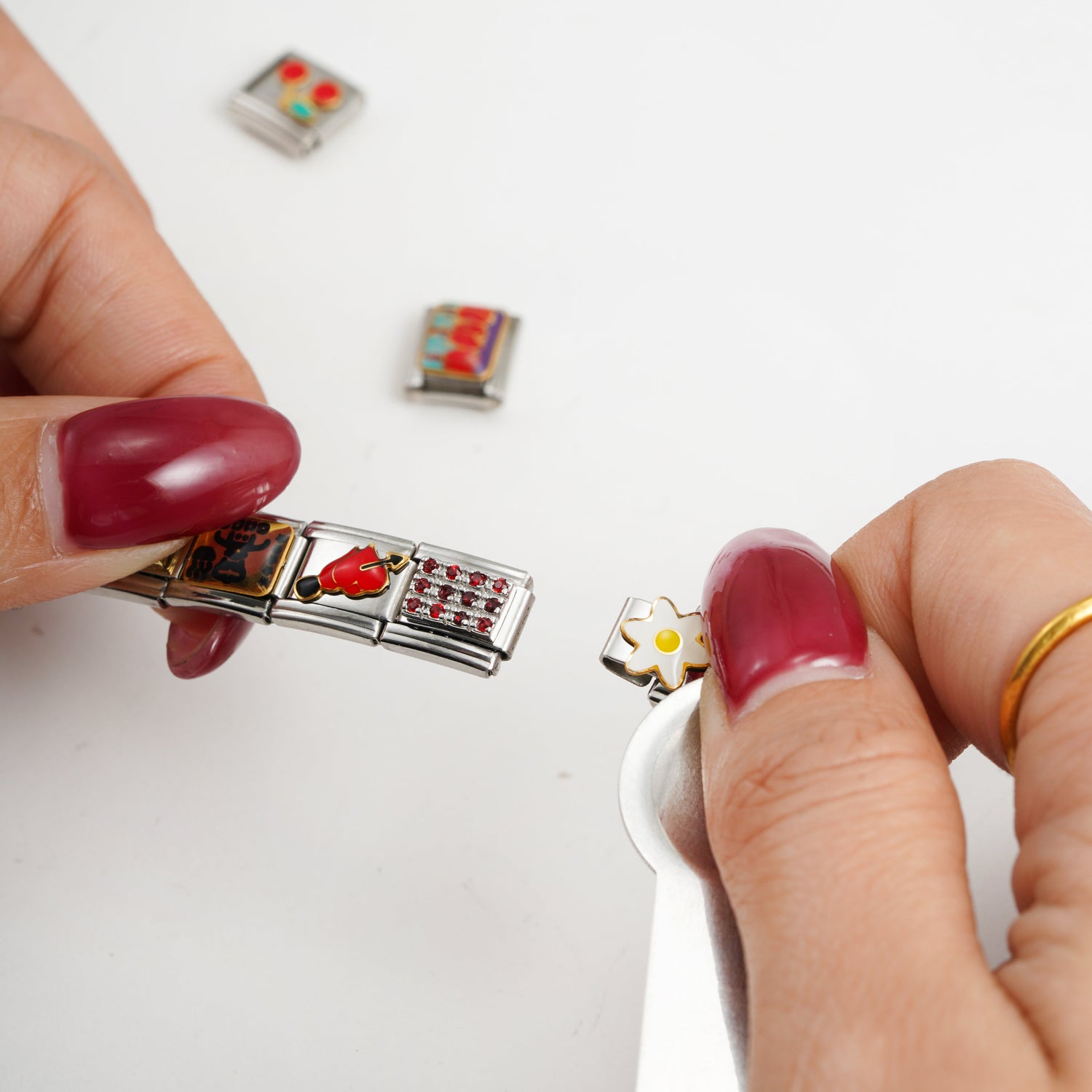 Hands attaching a small flower charm to an Italian charm bracelet using a metal tool